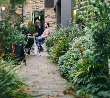 A person walking a dog on a garden path surrounded by lush greenery.