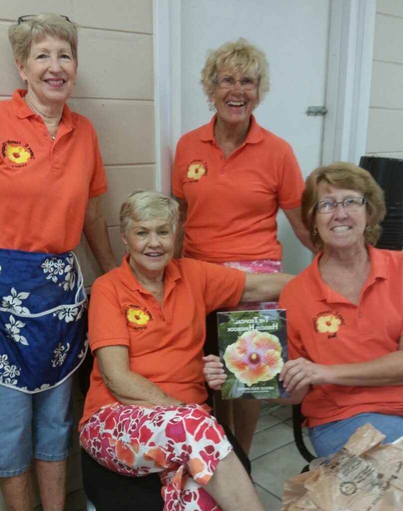 A group of women in matching orange shirts smiling and posing together.