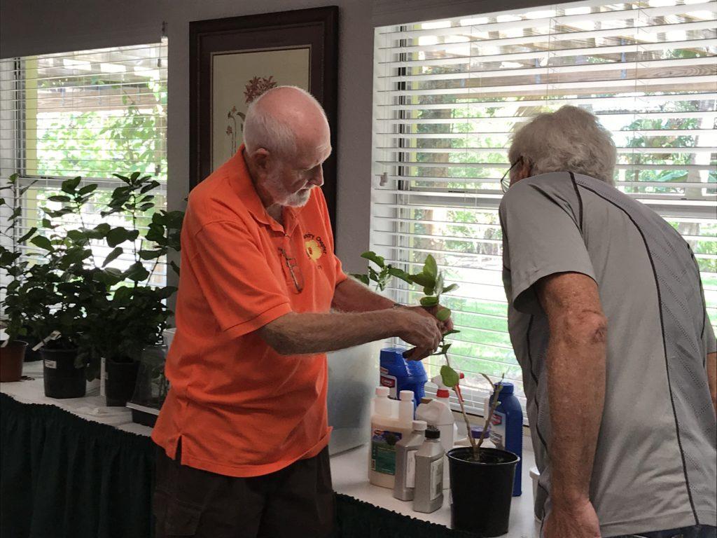 Two men in a kitchen, one wearing an orange shirt.