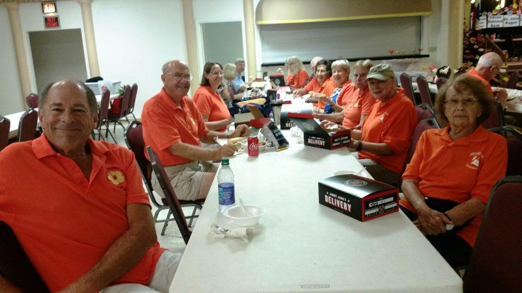 Group of men in red shirts gathered around a table with laptops and papers.