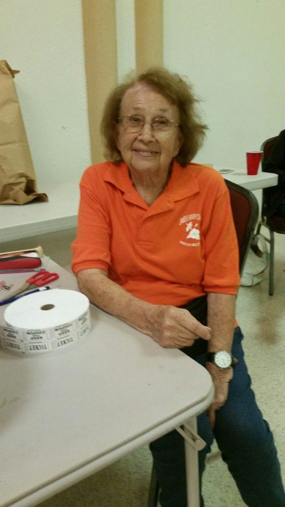 An elderly woman smiling while seated at a table with a cup of tea.