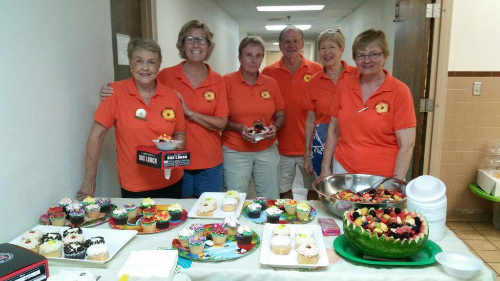 Group of people in orange shirts posing with food on a table.