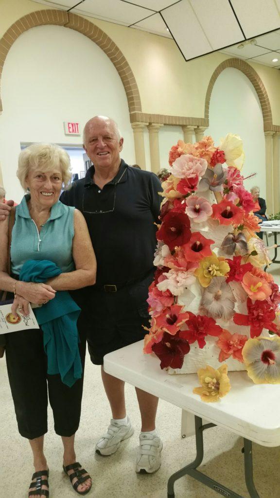 Elderly couple posing beside a colorful flower cake.