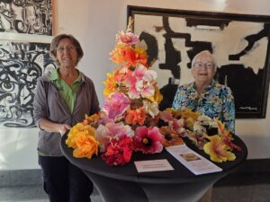 Two women smiling behind a table with colorful flower arrangements.