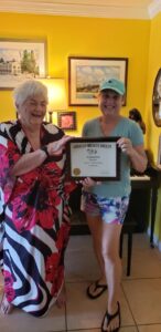Two women smiling, one holding a framed certificate.